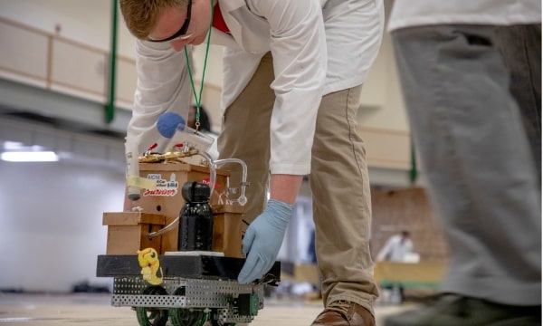 Student in laboratory attire placing Chem E car on the ground